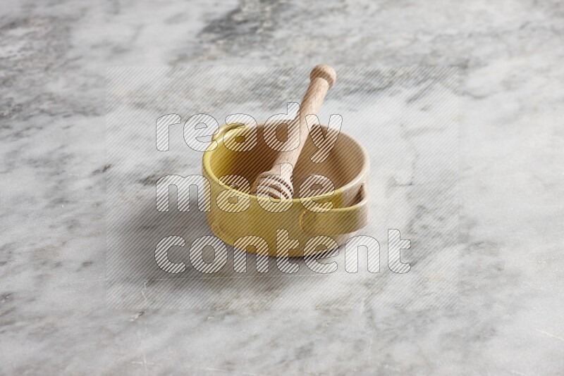 Multicolored pottery bowl with wooden honey dipper in it on grey marble background