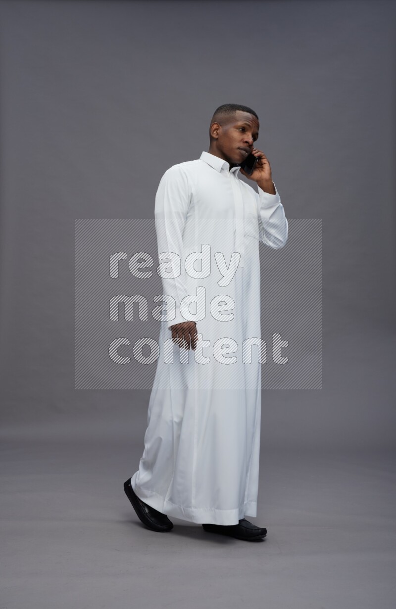 Saudi man wearing thob standing talking on phone on gray background