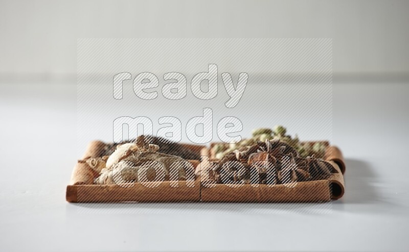 4 مربعات من أعواد القرفة ممتلئة بالشاي والهيل واليانسون والزنجبيل على أرضية بيضاء