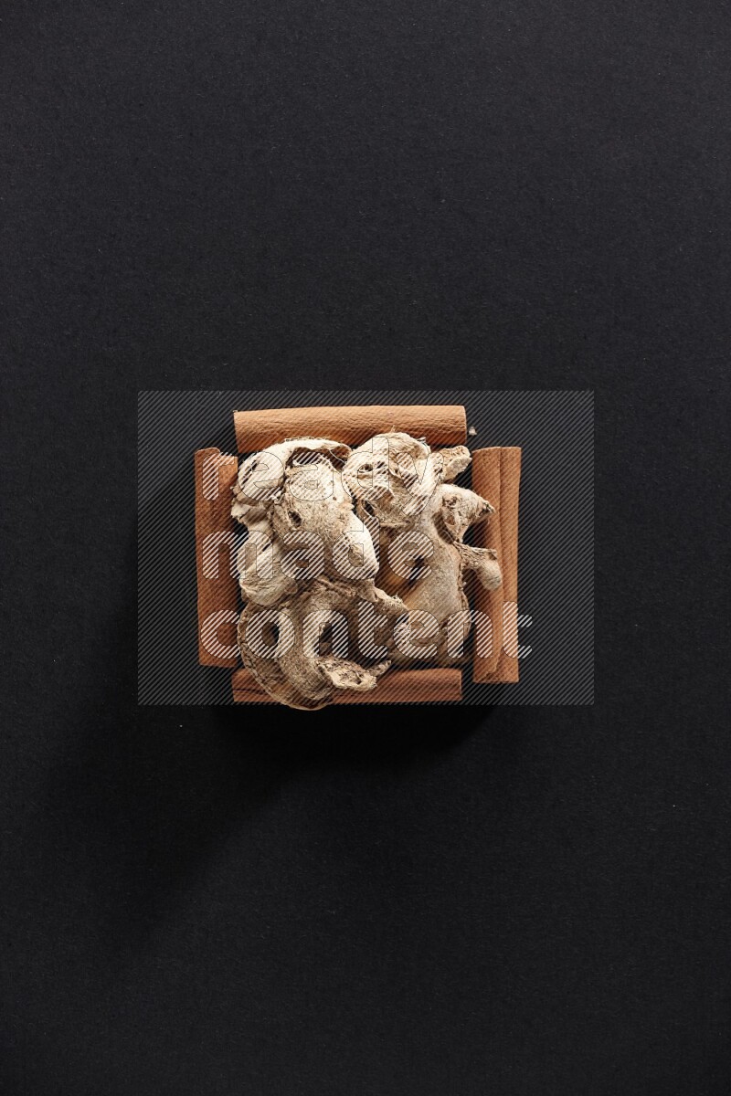 أربعة من أعواد القرفة مكونة شكل مربع بداخلها زنجبيل مجفف علي خلفية سوداء