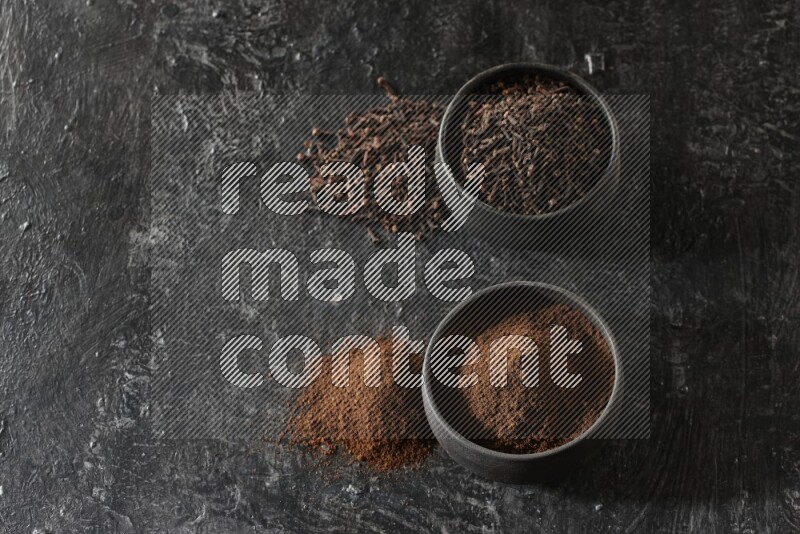 وعاءين من الفخار الأسود أحدهما ممتلئي بحبوب القرنفل والآخر ممتلئ ببودرة القرنفل على خلفية سوداء