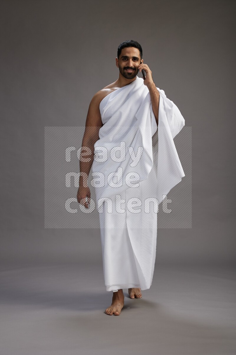 A man wearing Ehram Standing talking on phone on gray background