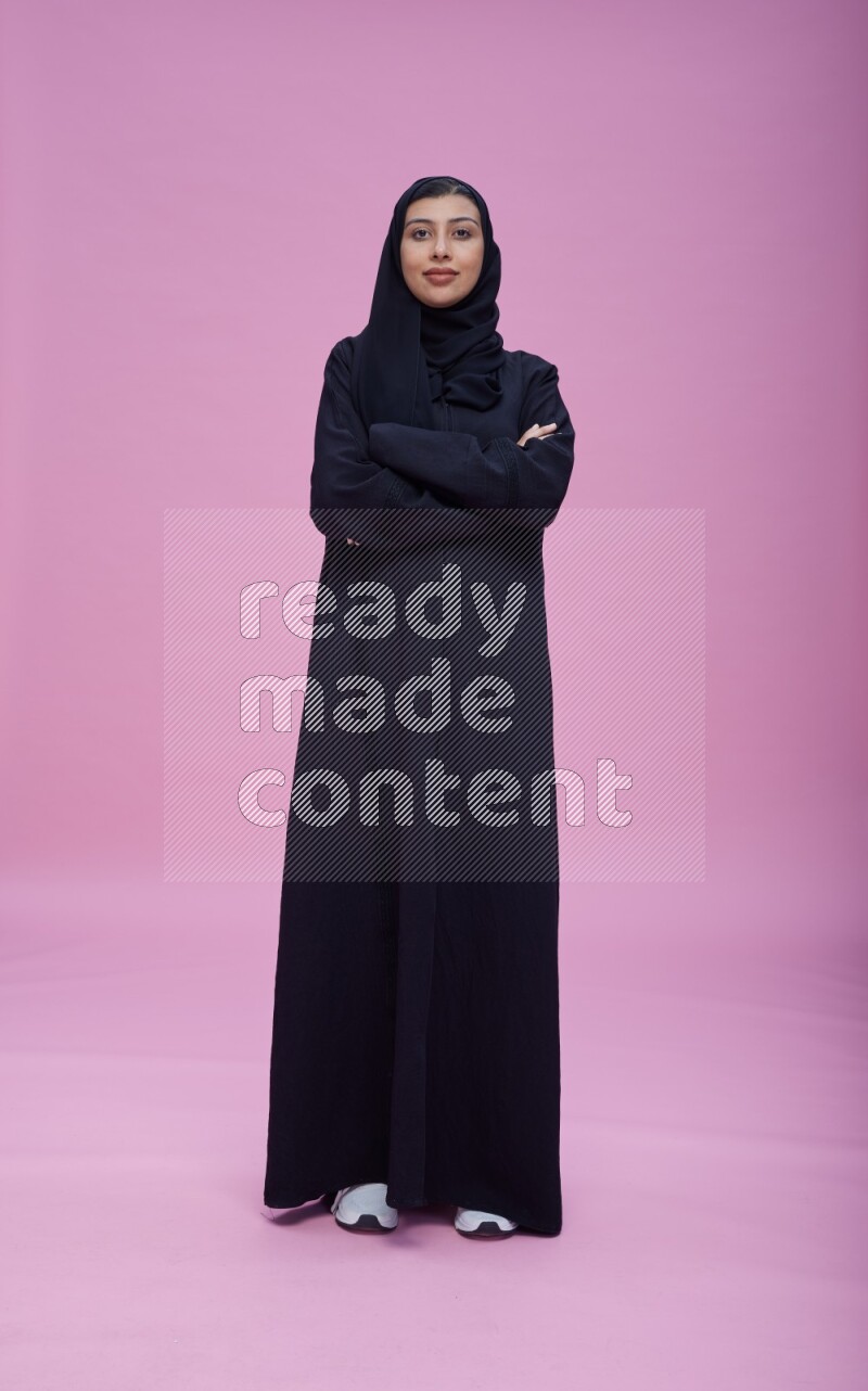 Saudi woman wearing Abaya standing with crossed arms on pink background