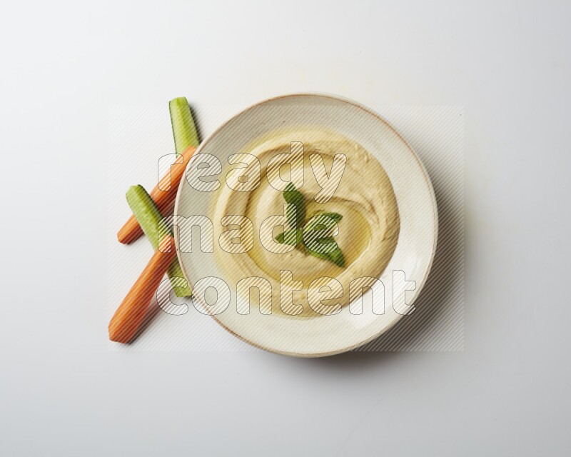 Hummus in a pottry plate garnished with mint  on a white background