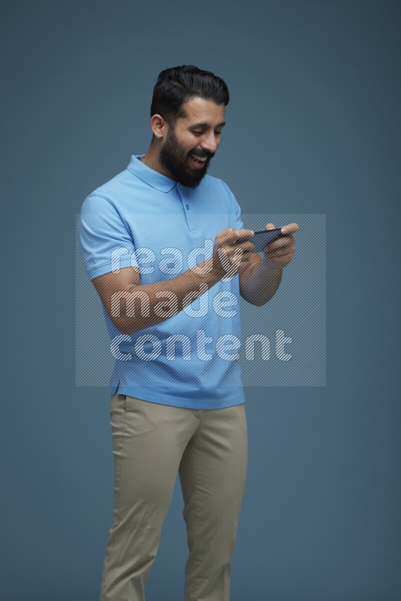 Man playing a game on his phone in a blue background wearing a Blue shirt