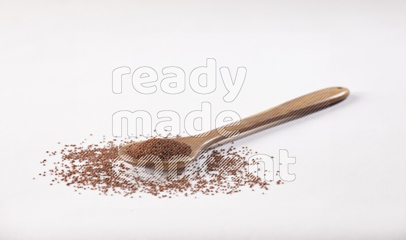 A wooden ladle full of garden cress seeds on a white flooring