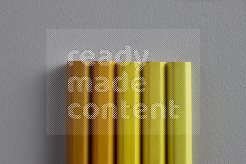 A collection of sharpened colored pencils arranged showcasing a gradient of yellow and orange hues on grey background