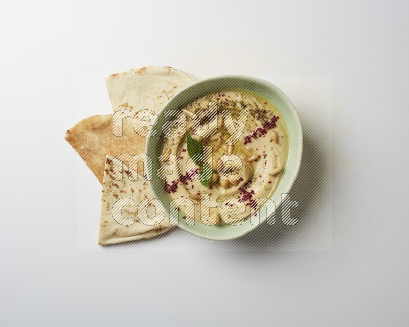 Hummus in a green plate garnished with zattar & sumak on a white background