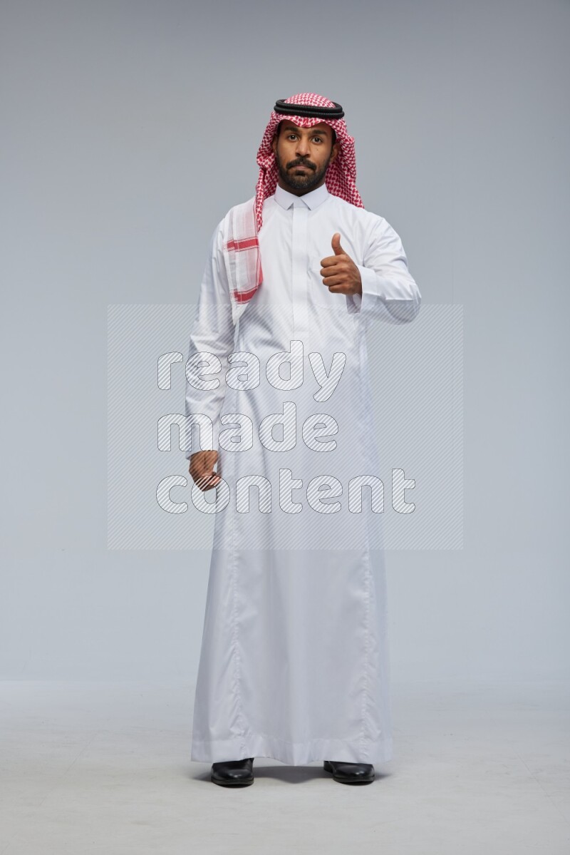 Saudi man Wearing Thob and shomag standing interacting with the camera on Gray background