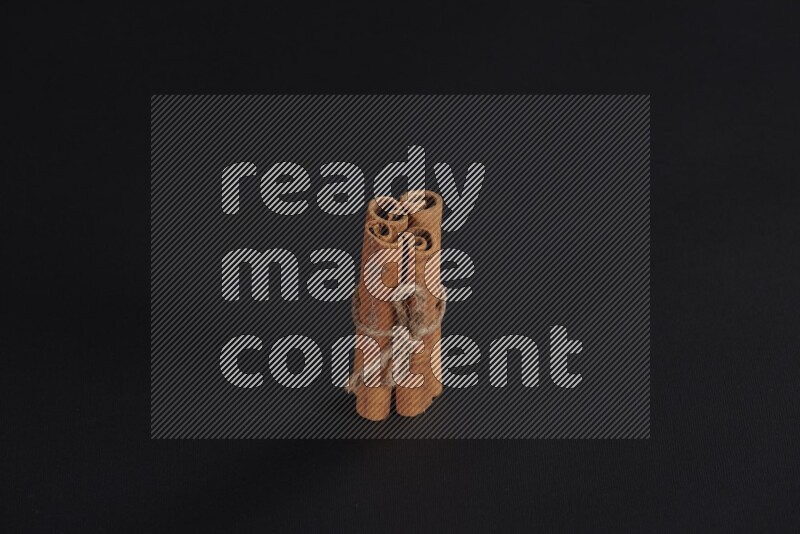 4 أعواد من القرفة مربوطة علي خلفية سوداء