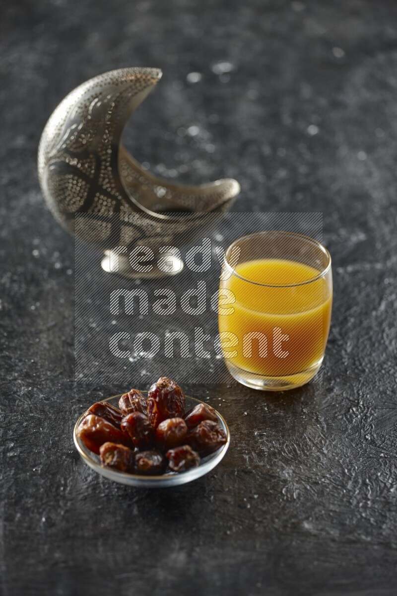 A silver lantern with different drinks, dates, nuts, prayer beads and quran on textured black background