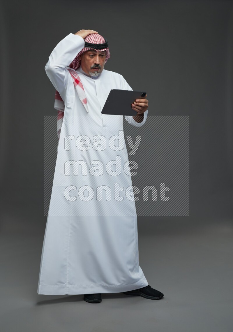 Saudi man with shomag Standing working on tablet on gray background