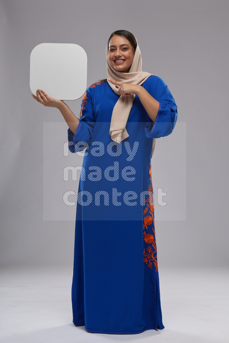 A Saudi woman standing wearing Jalabeya holding a social media sign