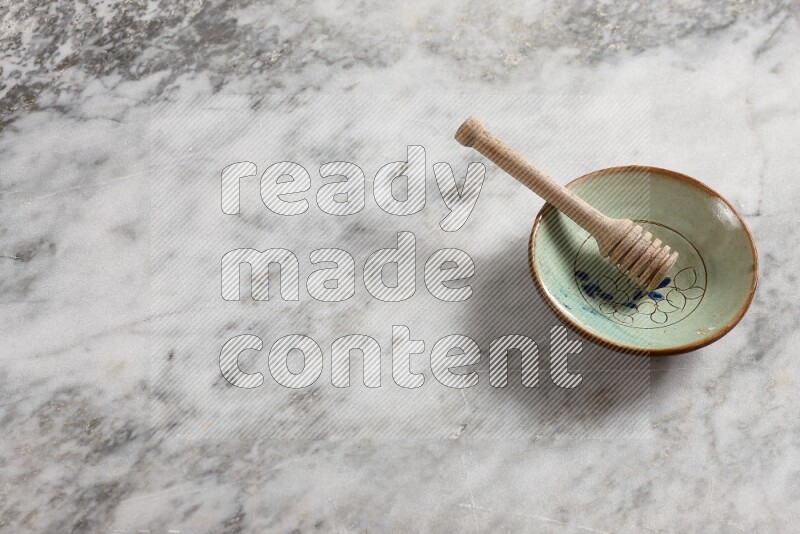 Decorative pottery plate with wooden honey dipper in it on grey marble background