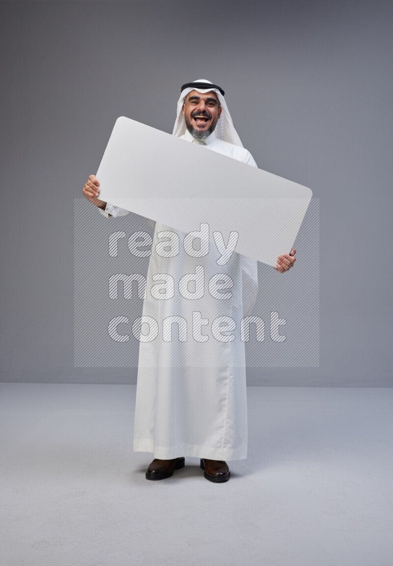 Saudi man Wearing Thob and white Shomag standing holding board on Gray background