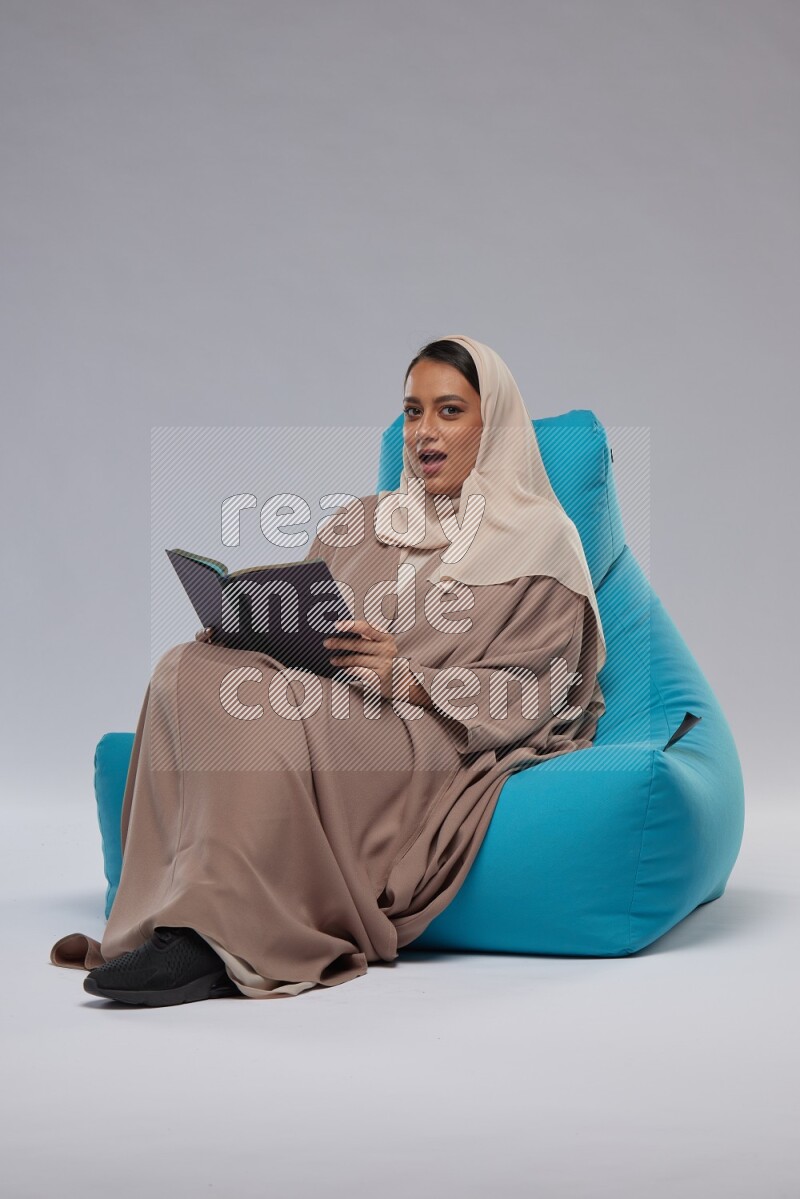 A woman sitting on a blue beanbag and reading a book