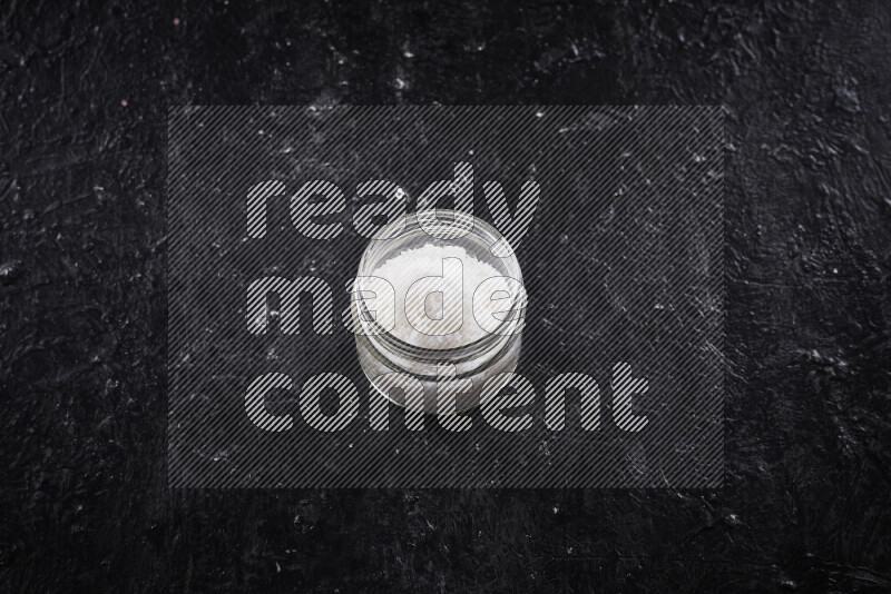 وعاء زجاجي ممتلئ بملح البحر الخشن على خلفية سوداء