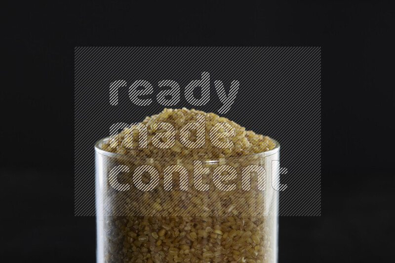 Coarse bulgur in a glass jar on black background
