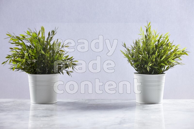 Two green artificial plants in white pot on grey marble background