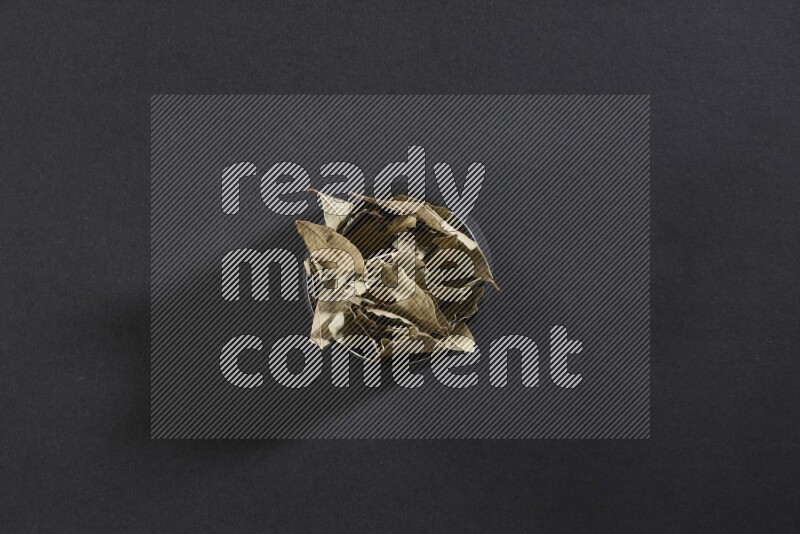 A black pottery bowl full of dried bay leaves on black flooring