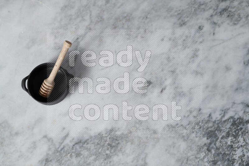 Black pottery bowl with wooden honey dipper in it on grey marble background
