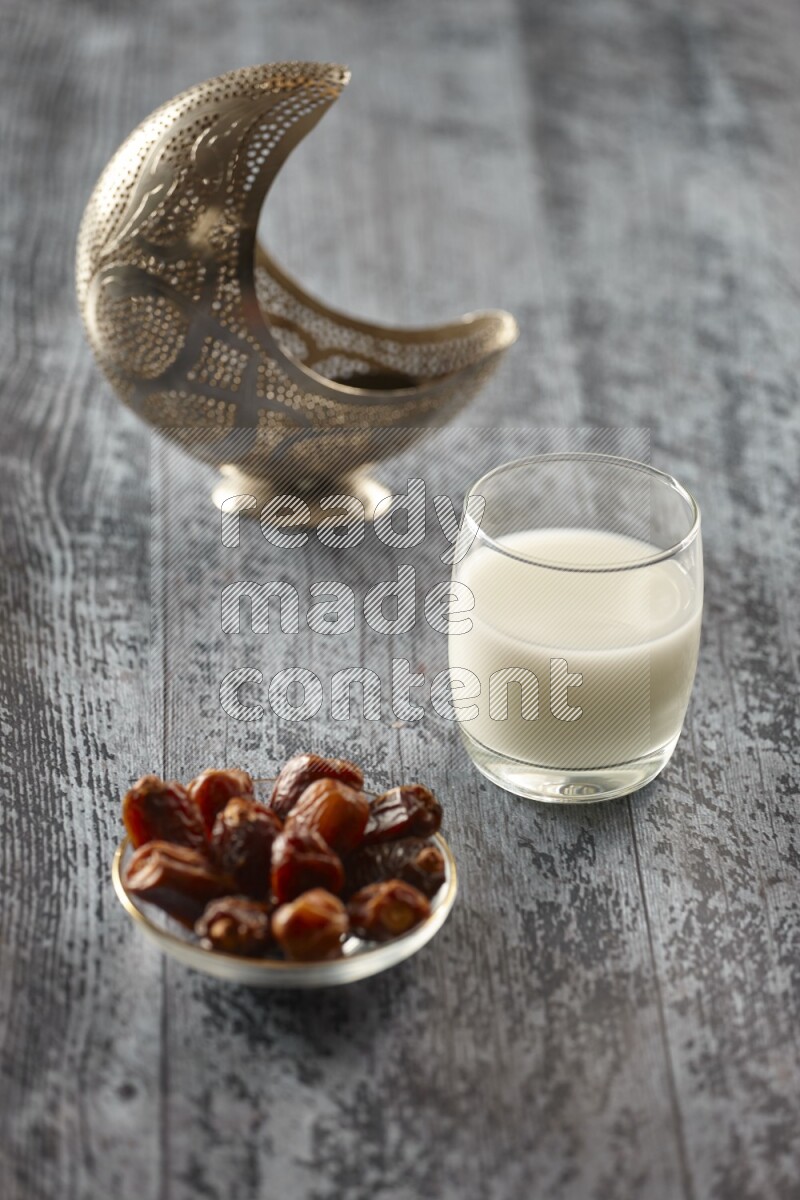 A silver lantern with different drinks, dates, nuts, prayer beads and quran on grey wooden background