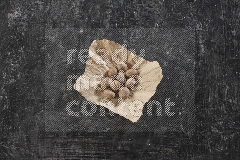 A crumpled piece of paper full of whole nutmeg seeds on a textured black flooring