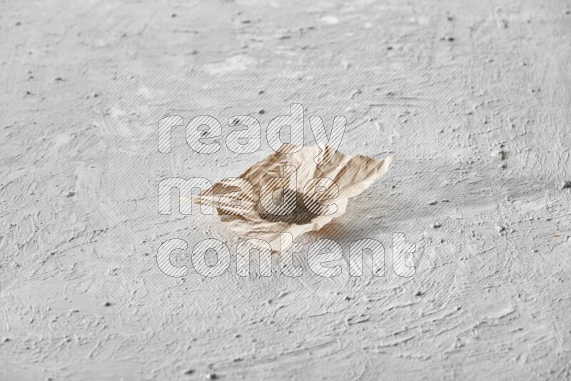 Black pepper powder on a crumpled paper on a textured white flooring