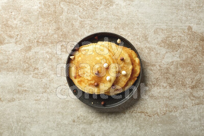 Three stacked chocolate chips pancakes in a black plate on beige background