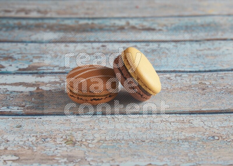 45º Shot of of two assorted Brown Irish Cream, and Yellow, and Brown Chai Latte macarons  on light blue background