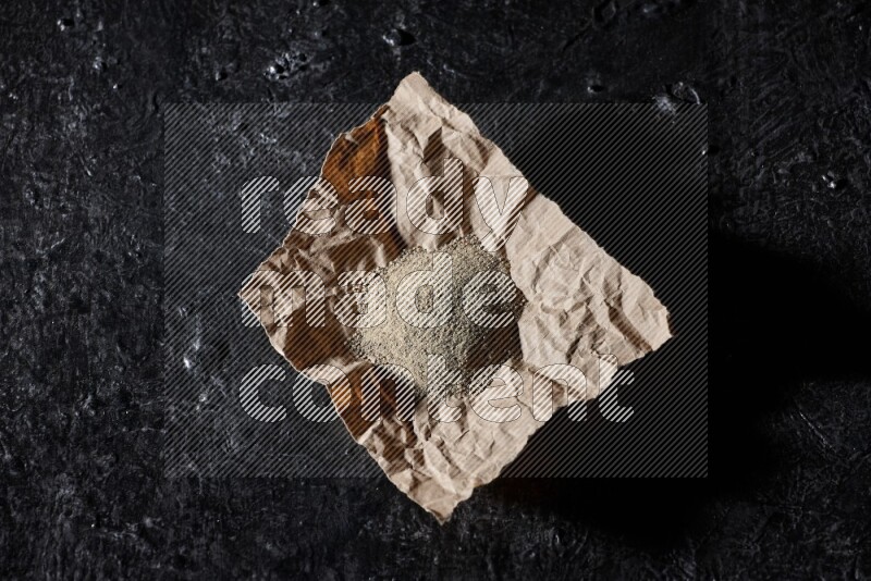 White pepper powder in a crumpled paper on textured black flooring