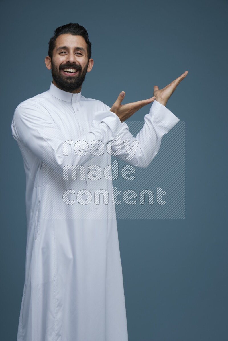A man pointing in a blue background wearing Saudi Thob