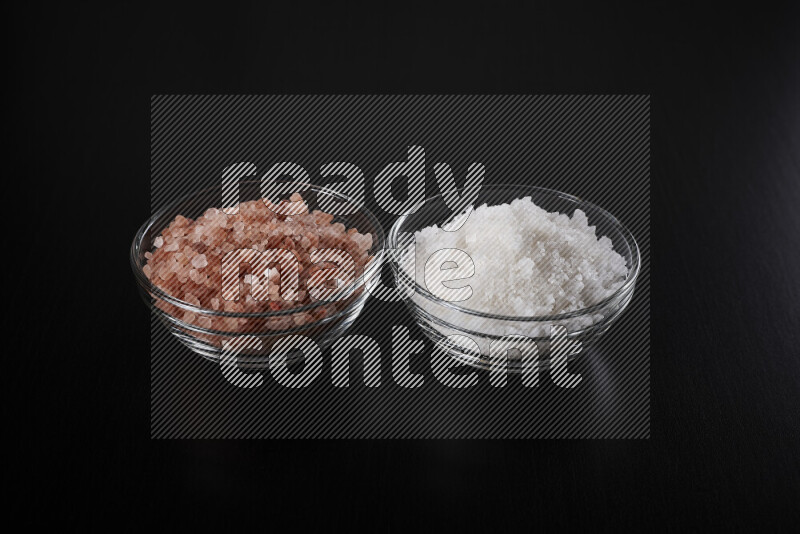 2 وعاء زجاجي احدهمها ممتلئ بملح الهيمالايا والأخر بالملح الأبيض على خلفية سوداء