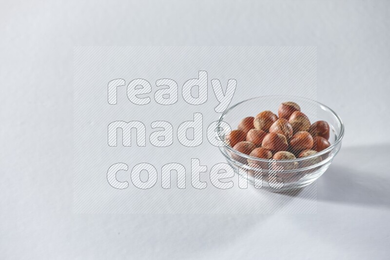A glass bowl full of hazelnuts on a white background in different angles
