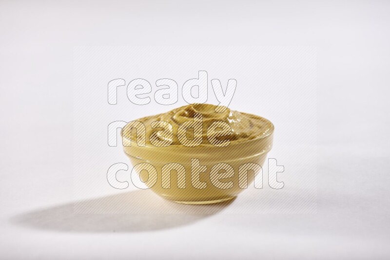 A glass bowl full of mustard paste on a white flooring