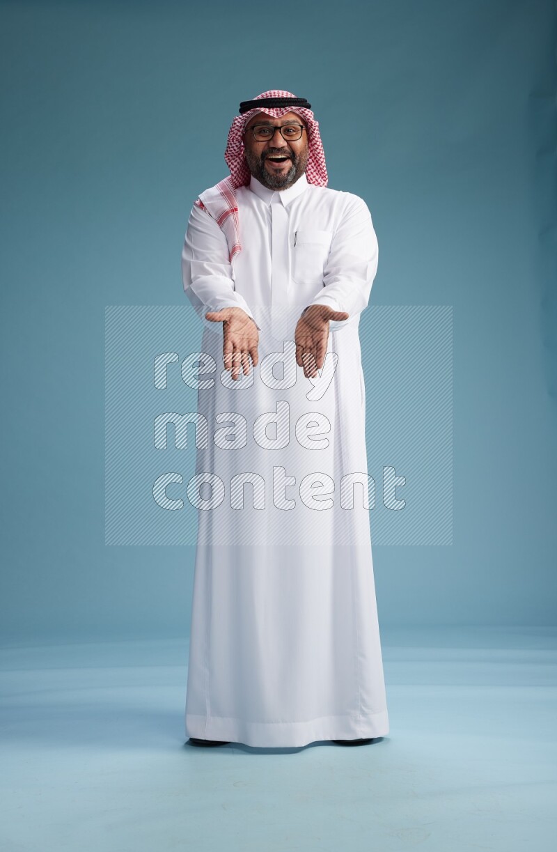 Saudi Man with shimag Standing Interacting with the camera on blue background