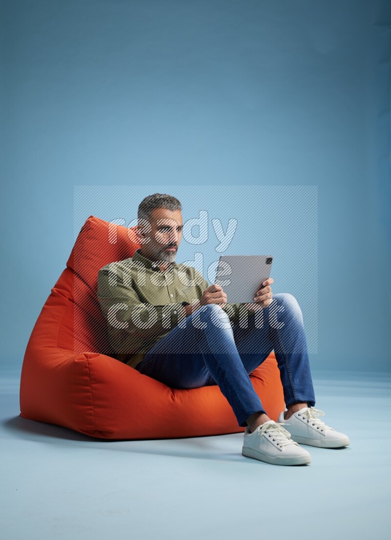 A man sitting on an orange beanbag and working on tablet