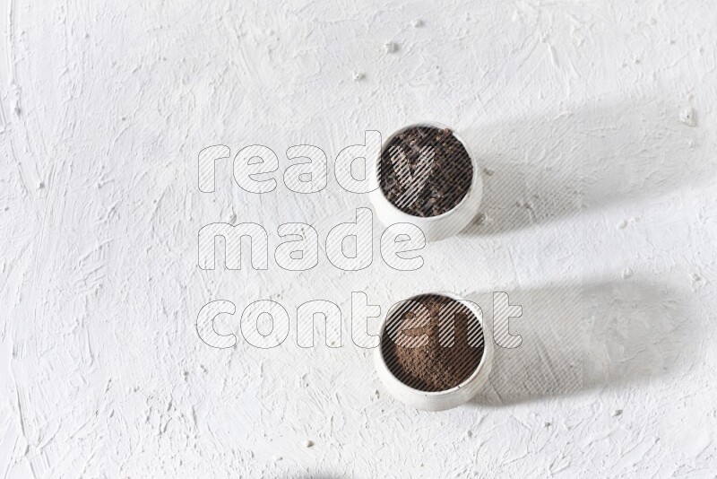 2 Beige ceramic bowls, one full of cloves and the other full of powder on textured white flooring