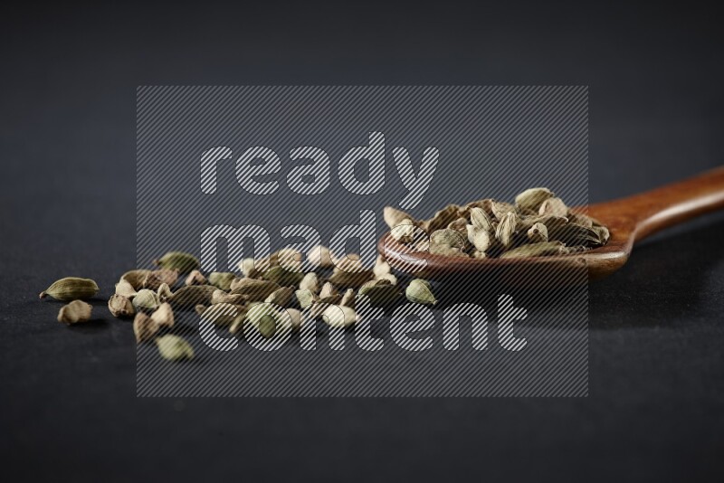 مغرفة خشبية ممتلئة بالهيل على خلفية سوداء