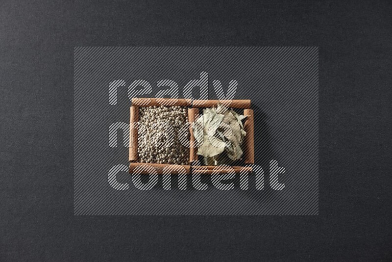 مربعان من أعواد القرفة ممتلئان بحبوب الفلفل الأبيض وأوراق الغار علي خلفية سوداء