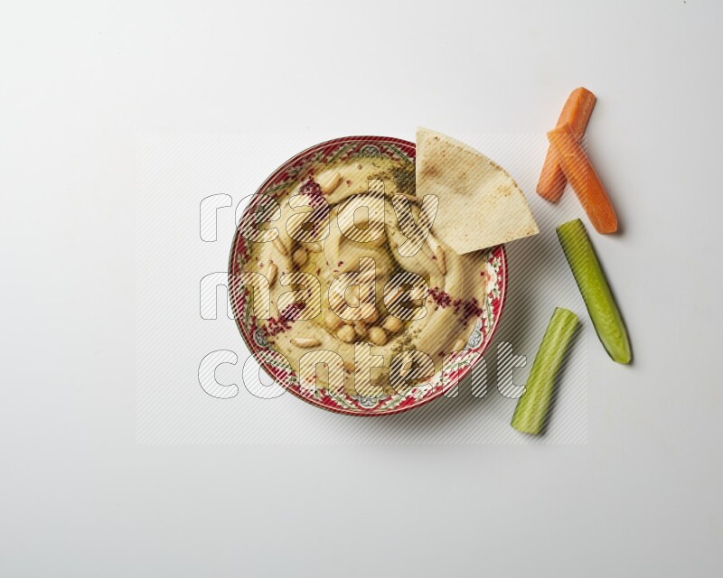 Hummus in a red plate with patterns garnished with zaatar & sumak on a white background