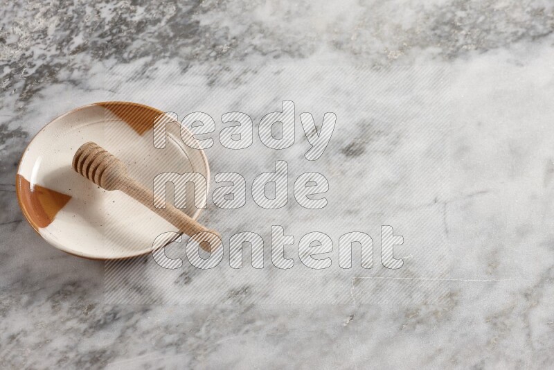 طبق فخاري متعدد الألوان مع ملعقة عسل خشبية بداخله على خلفية من الرخام الرمادي