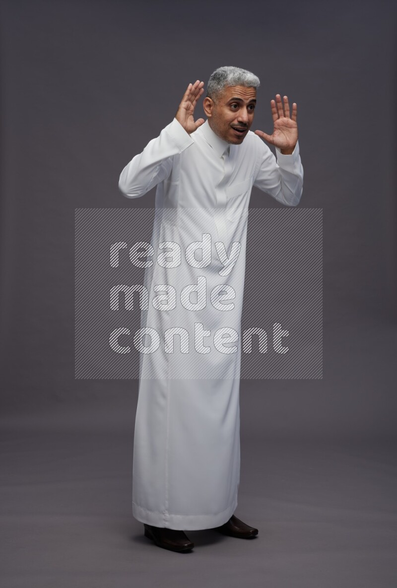 Saudi man wearing thob standing hands behind head on gray background