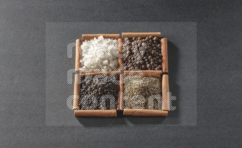 4 مربعات من عيدان القرفة ممتلئة بحبوب الفلفل الأسود والكمون وبهار الفلفل الحلو والملح الأبيض على أرضية سوداء