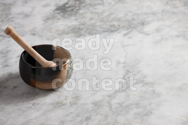 Multicolored pottery bowl with wooden honey dipper in it on grey marble background