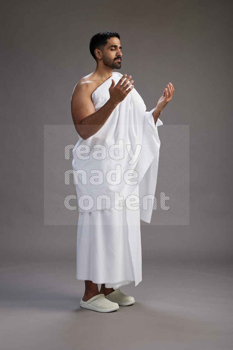 A man wearing Ehram Standing performing dua'a on gray background