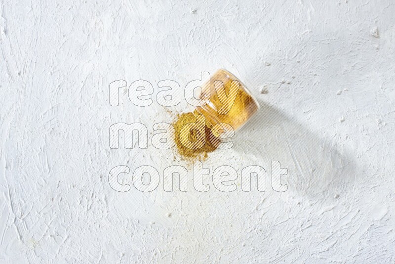 وعاء زجاجي مقلوب ممتلئ ببودرة الكركم والبودرة سقطت منه على خلفية بيضاء