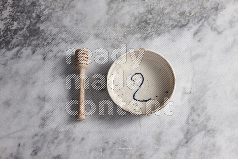 Multicolored pottery bowl with wooden honey dipper on the side on grey marble background