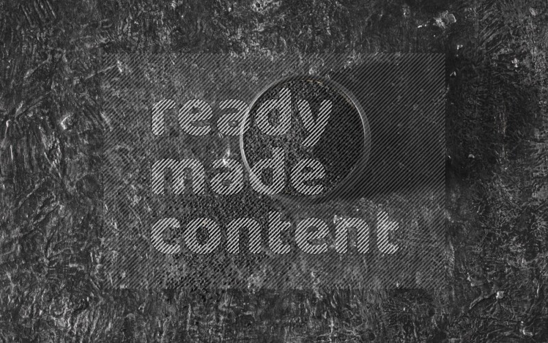 A black pottery bowl full of black seeds on a textured black flooring