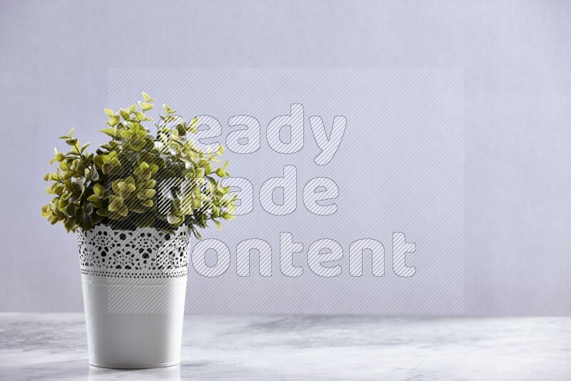 Green artificial plant in white decorative pot on grey marble background
